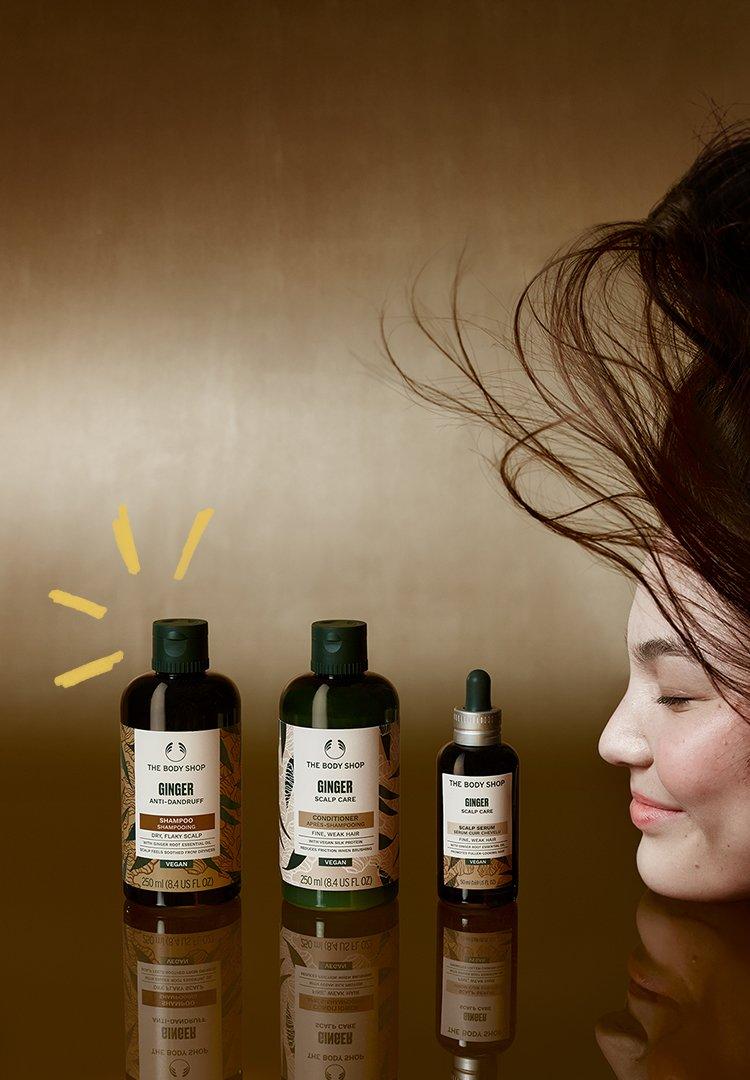 A Ginger haircare range, a bottle of shampoo, a bottle of conditioner and a serum on a table with ginger