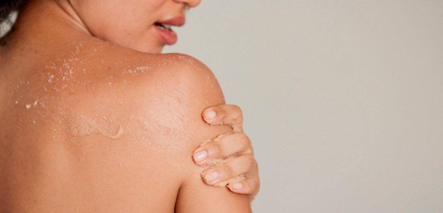 Mujer aplicando un exfoliante corporal en la espalda