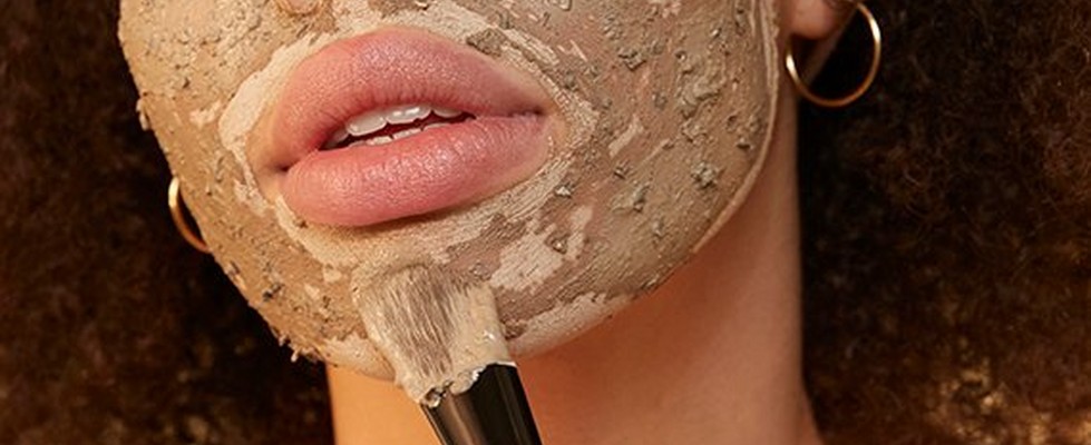 Woman wearing a white headband and applying a face mask with a brush Woman wearing a white headband and applying a face mask with a brush