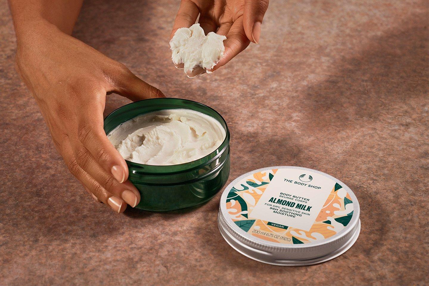Model scooping Almond Milk body butter from tub