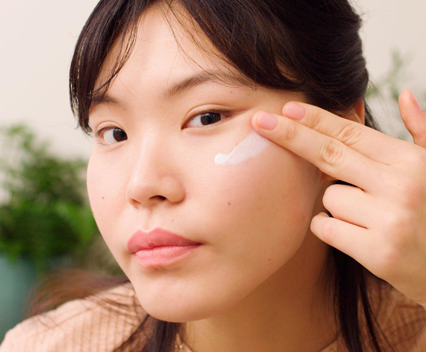 Model applying white skincare product to face