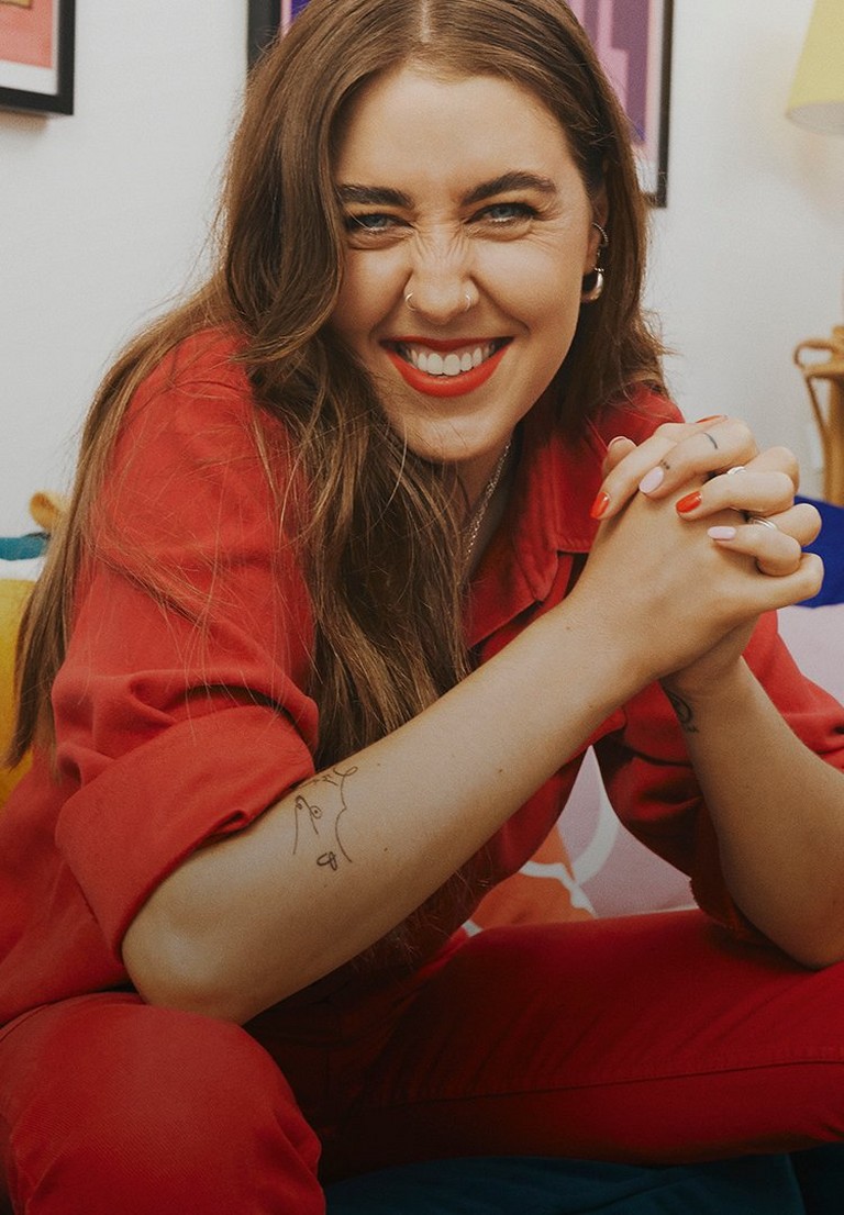 Gina Martin sat on a sofa wearing a red jumpsuit Gina Martin sat on a sofa wearing a red jumpsuit