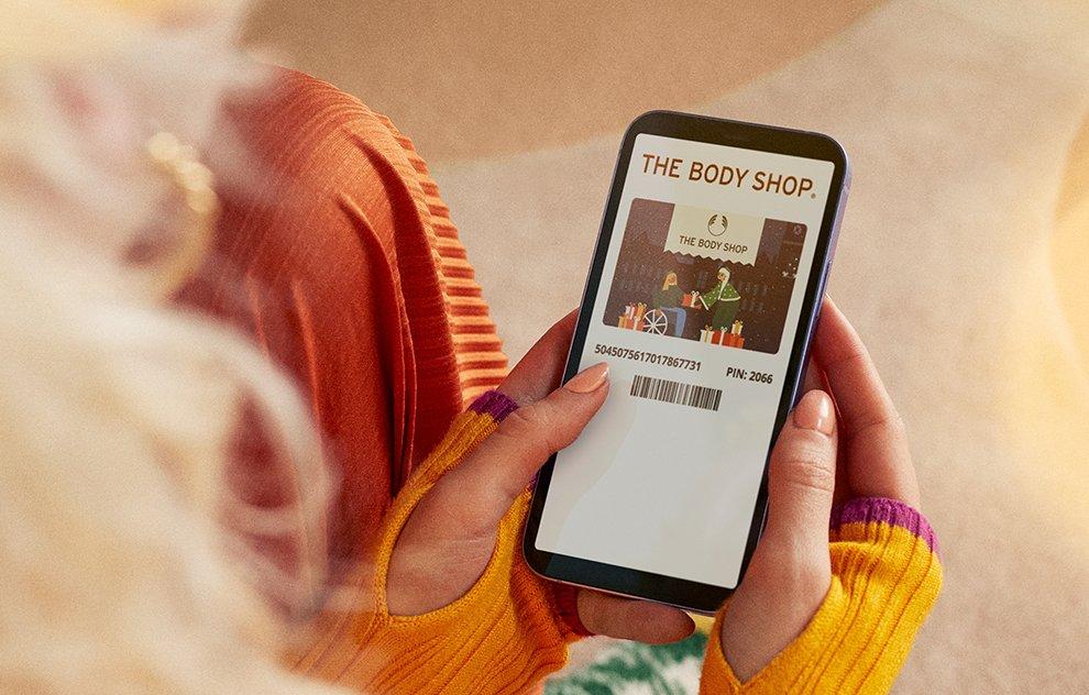 Image of woman holding a mobile phone, with a The Body Shop gift card on the screen