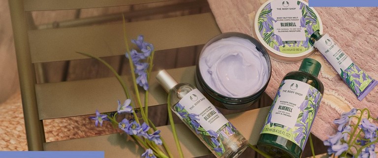 A range of four limited edition bluebell products laying down on a wooden table with some bluebell flowers next to them.