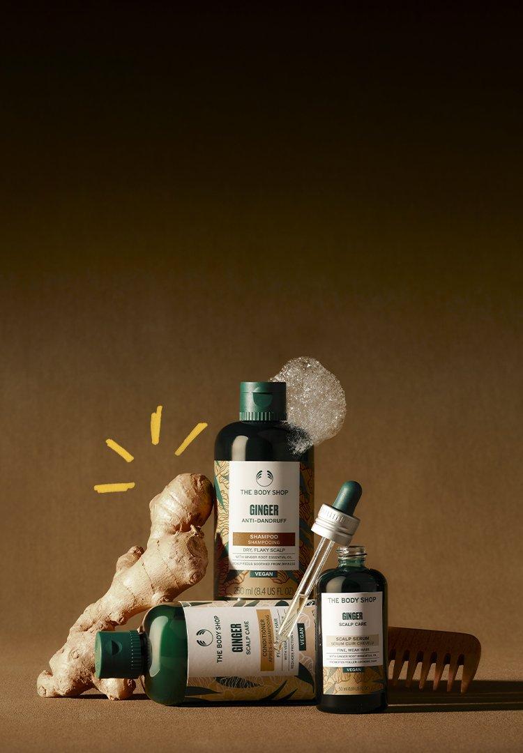 A Ginger haircare range, a bottle of shampoo, a bottle of conditioner and a serum on a table with ginger