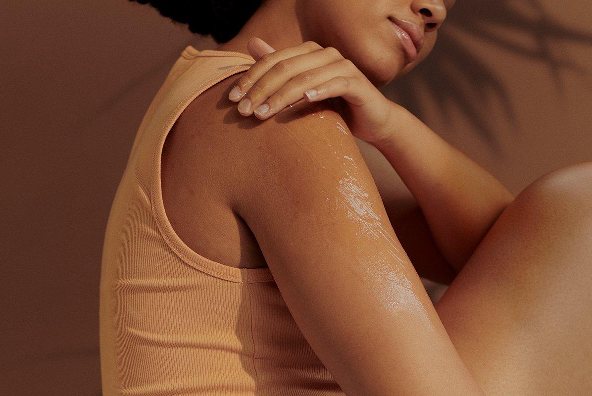 a woman sitting and applying lotion on her arm