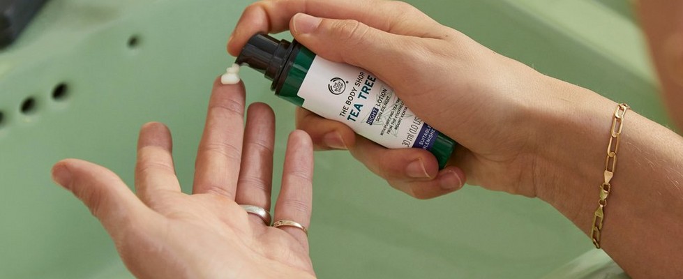 Hands pumping The Body Shop Tea Tree Night Lotion from bottle Hands pumping The Body Shop Tea Tree Night Lotion from bottle